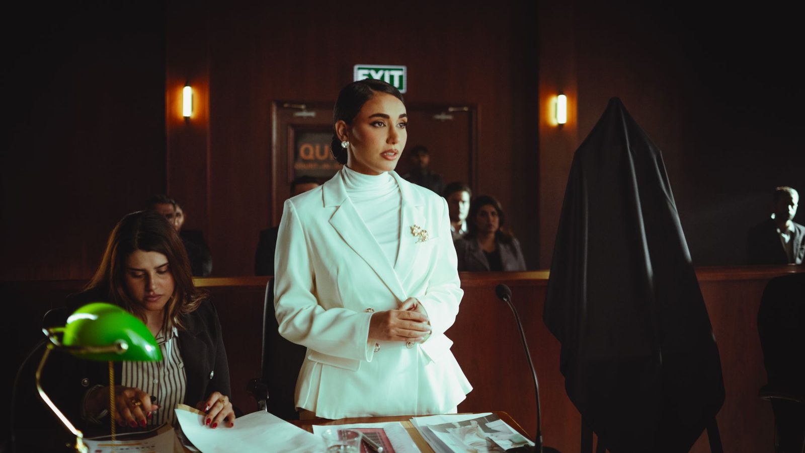A confident professional woman stands in a courtroom, projecting legal authority.