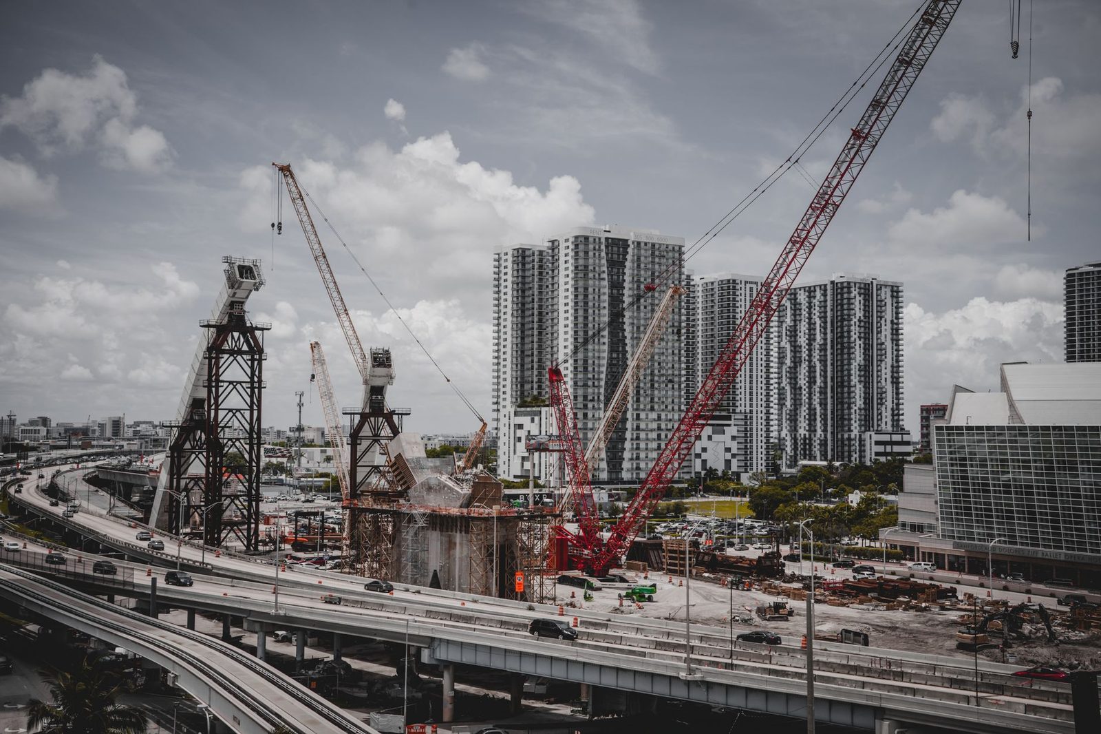 A construction site with cranes beside high-rise buildings under a cloudy sky.