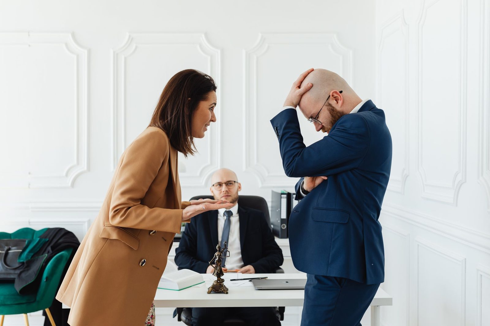 A couple argues across a desk in a law office while their attorney looks on.