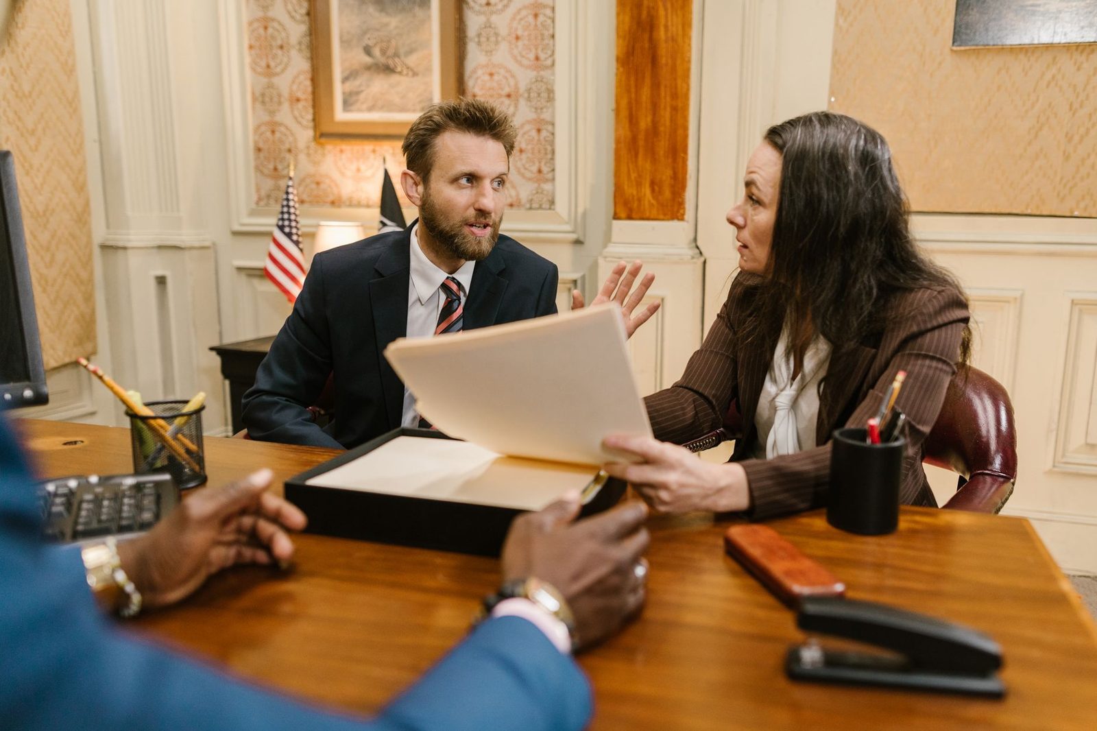 A diverse group of professionals in business attire meets around a conference table reviewing documents.