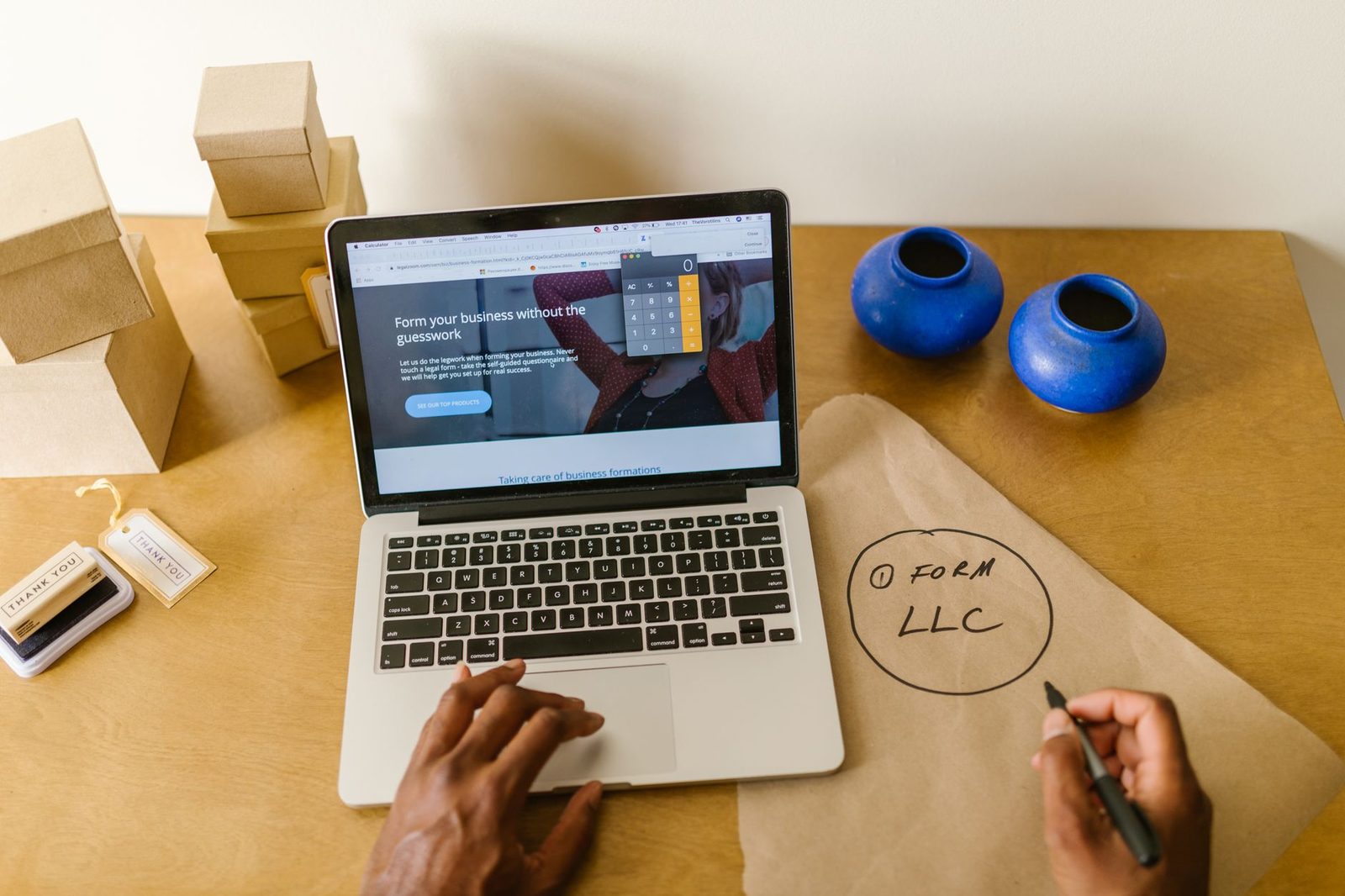 A laptop, shipping boxes, and handwritten LLC notes on a desk in a small business startup workspace.