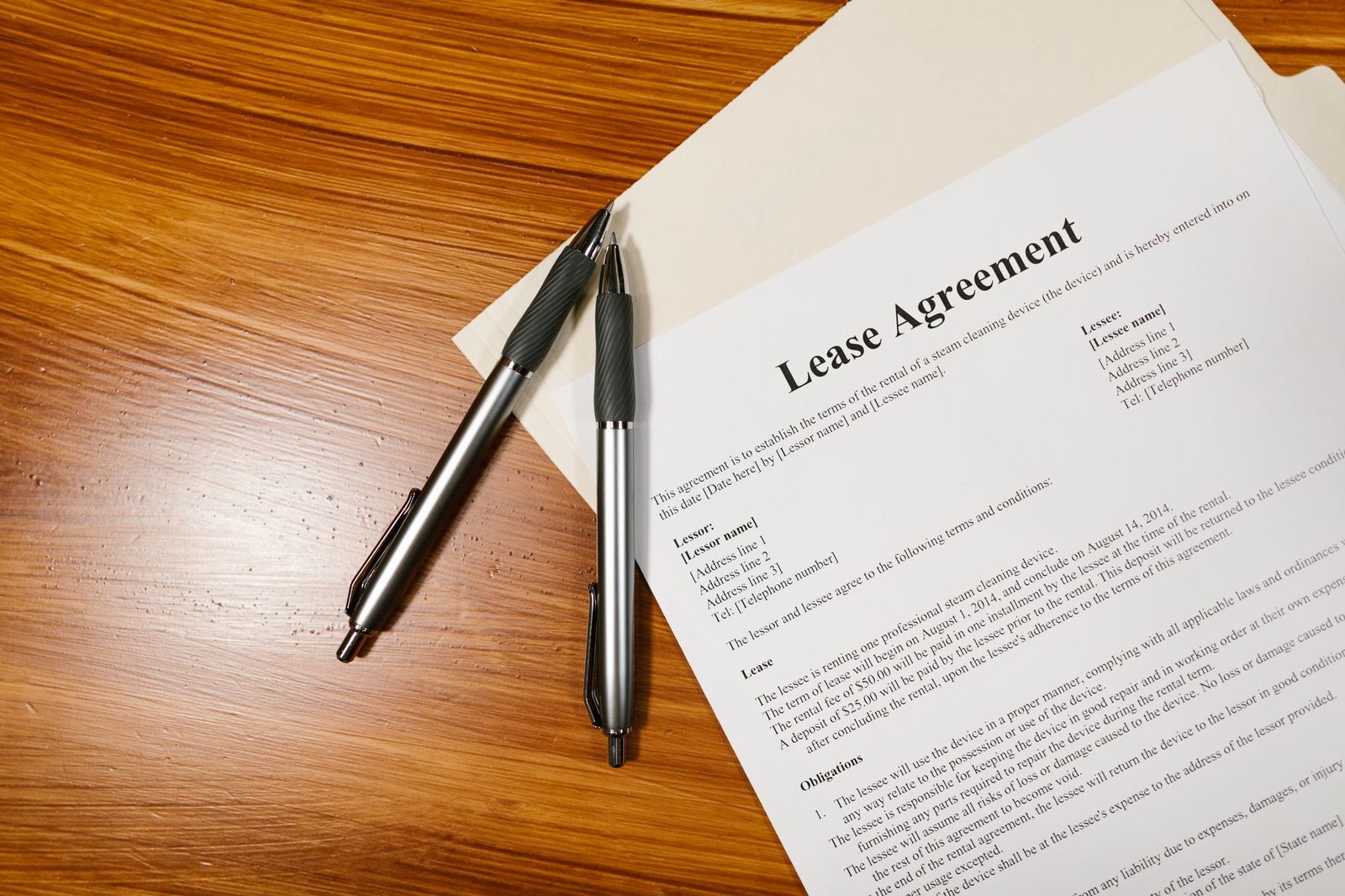 A lease agreement and two pens rest on a wooden desk, viewed from above.