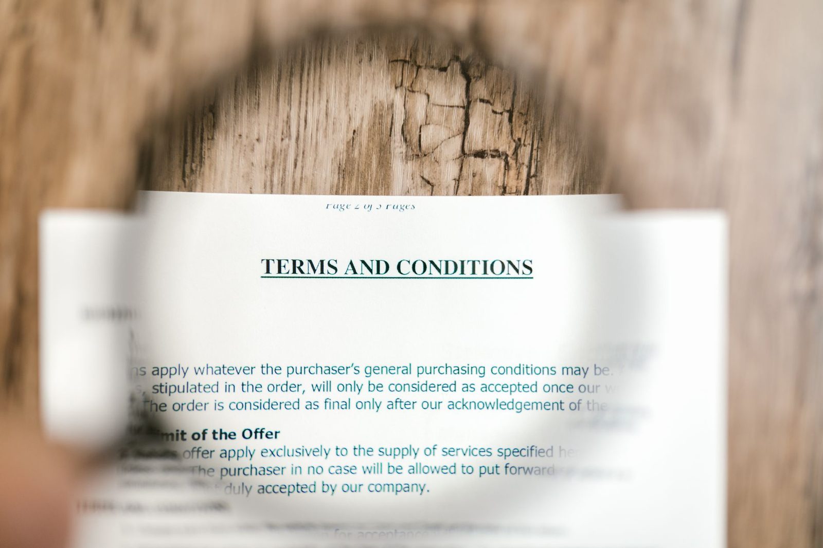 A magnifying glass held over a printed terms and conditions document resting on a wooden desk.
