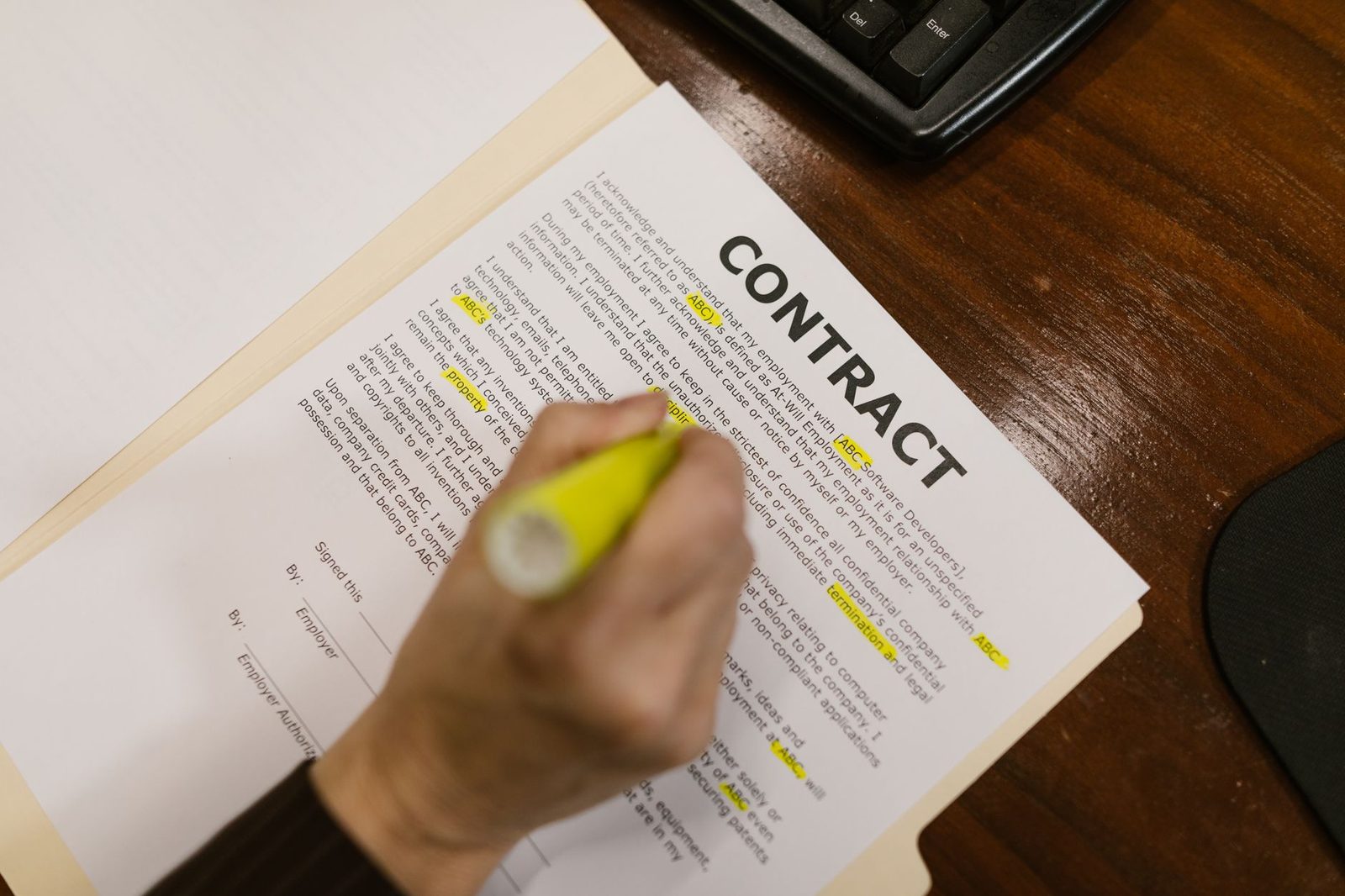 A person highlights a clause in a contract on a wooden office desk.