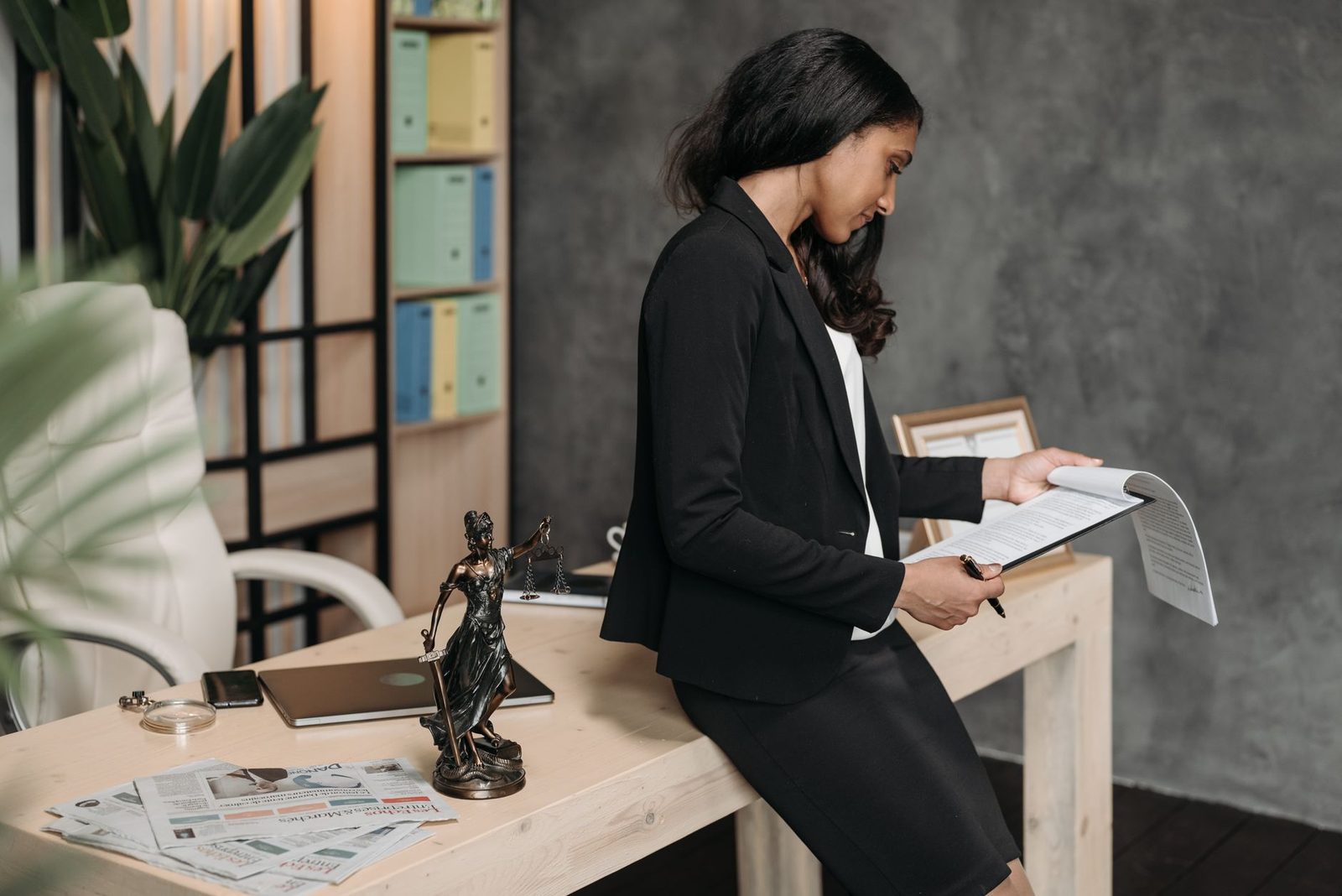 A professional woman in a business suit reviews legal documents at an office desk.