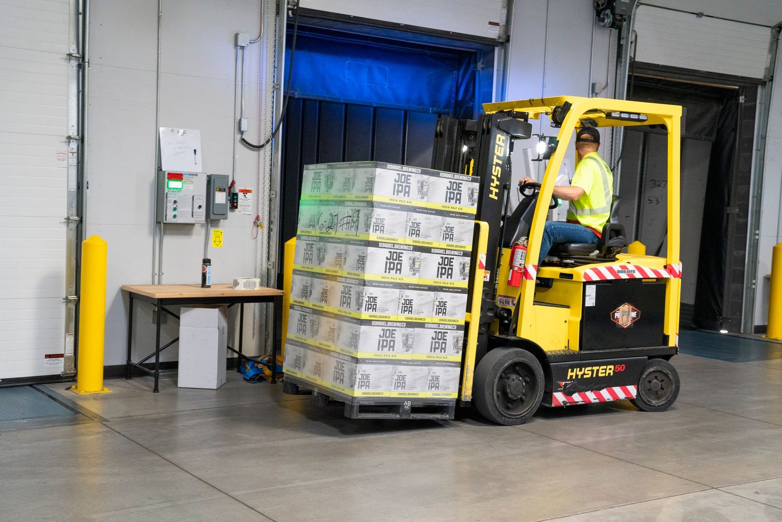 A warehouse worker drives a forklift to move stacked goods inside a storage facility.