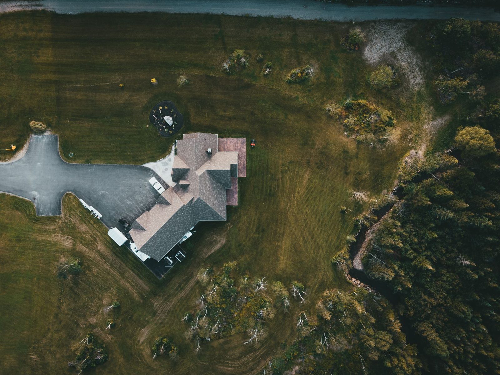 Aerial view of a suburban house surrounded by lush greenery and a driveway.
