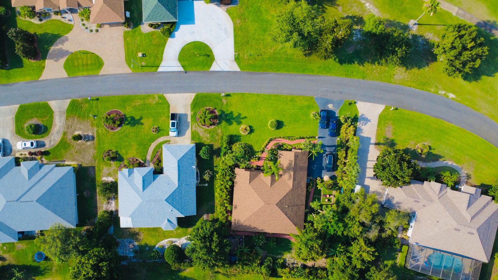 Aerial view of a suburban neighborhood with rows of houses, paved driveways, and green lawns.