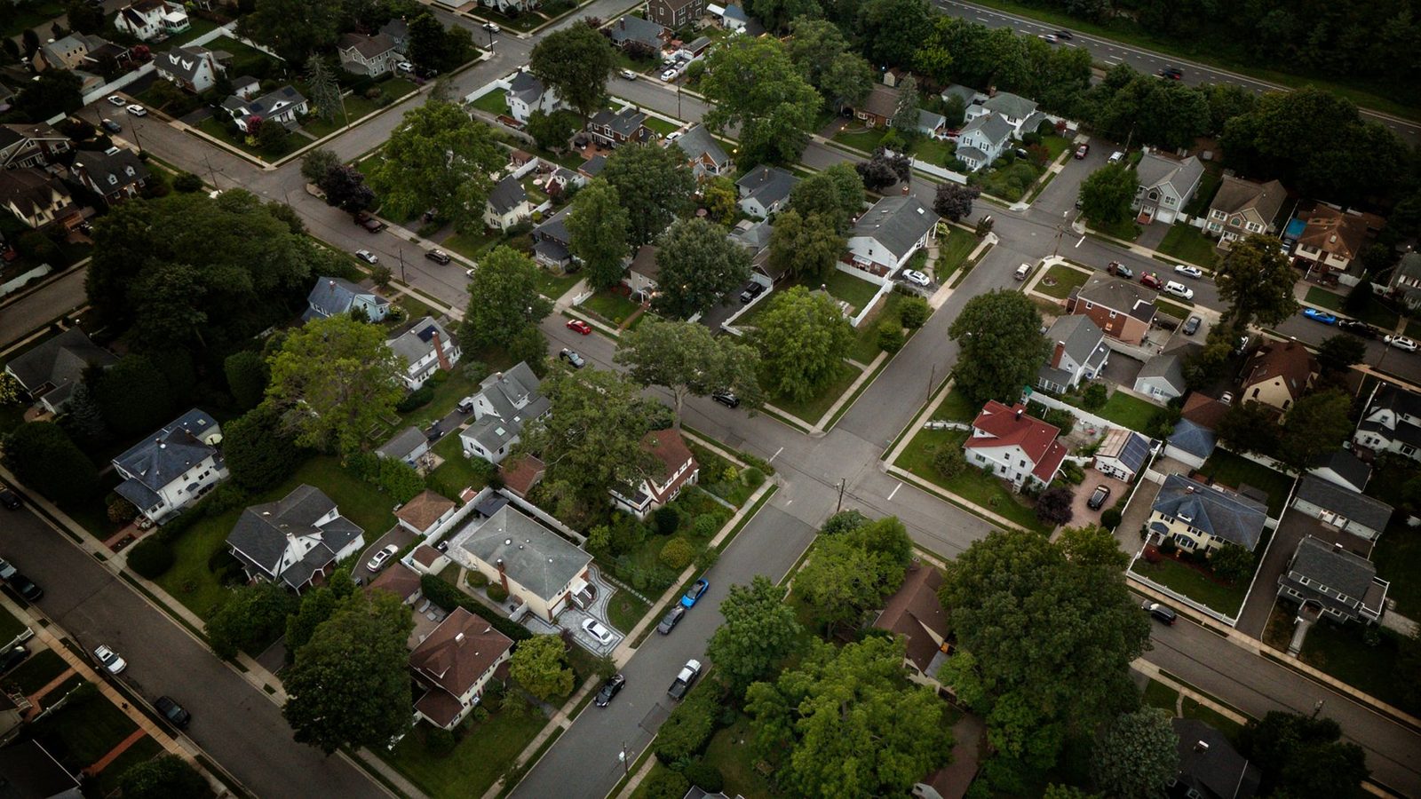 Aerial view of a suburban neighborhood with rows of houses surrounded by lush green trees.