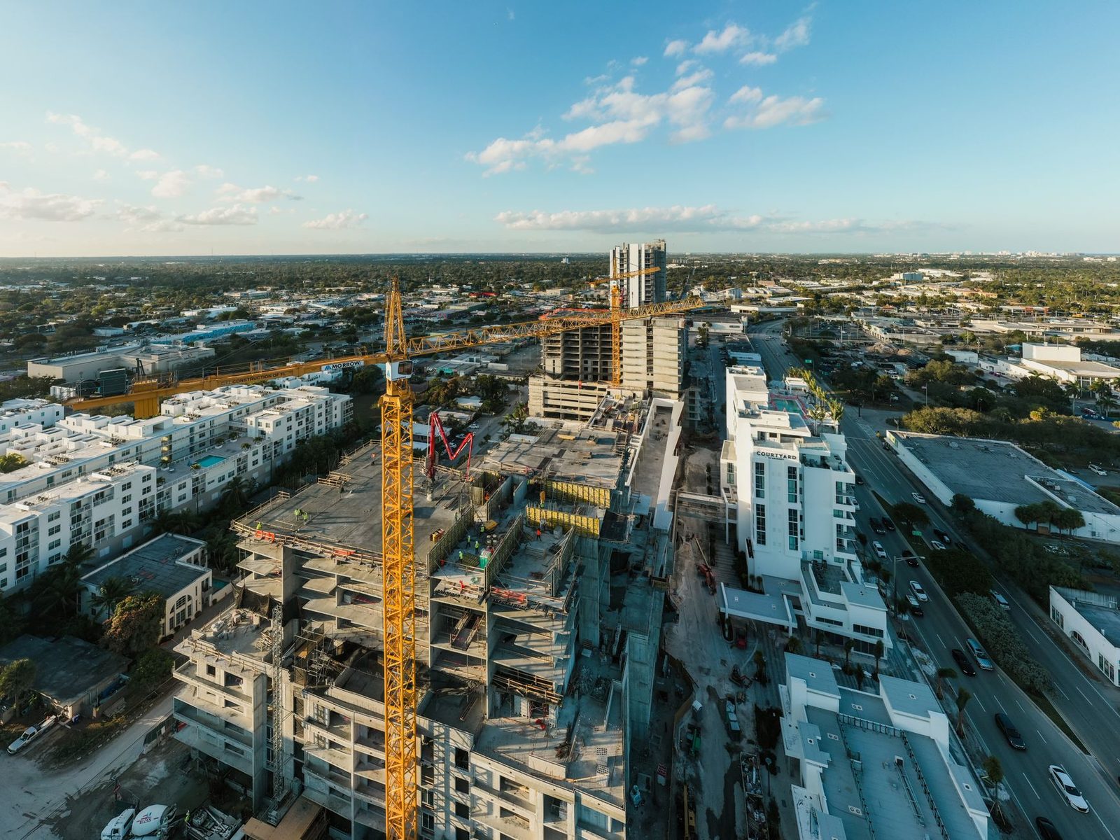 Aerial view of a construction site with a tower crane rising above a residential district in a modern city under a cloudy blue sky.