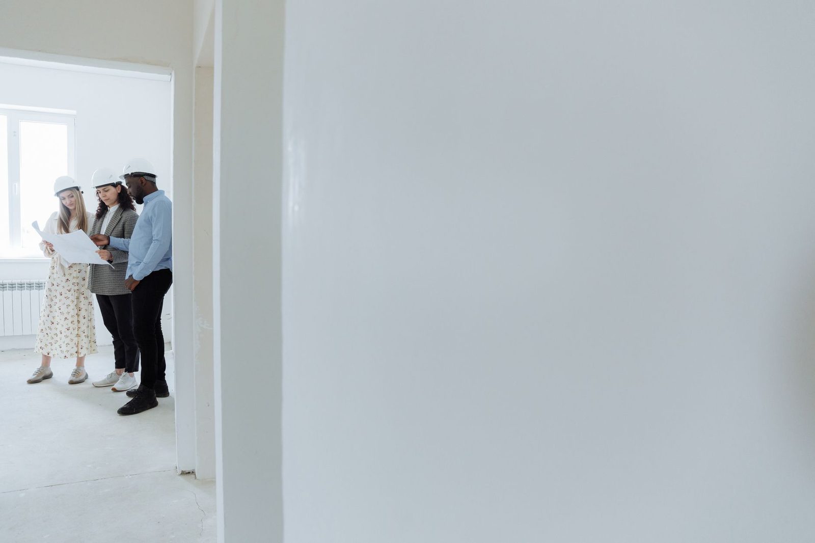 Architects in hard hats review blueprints at a construction site.