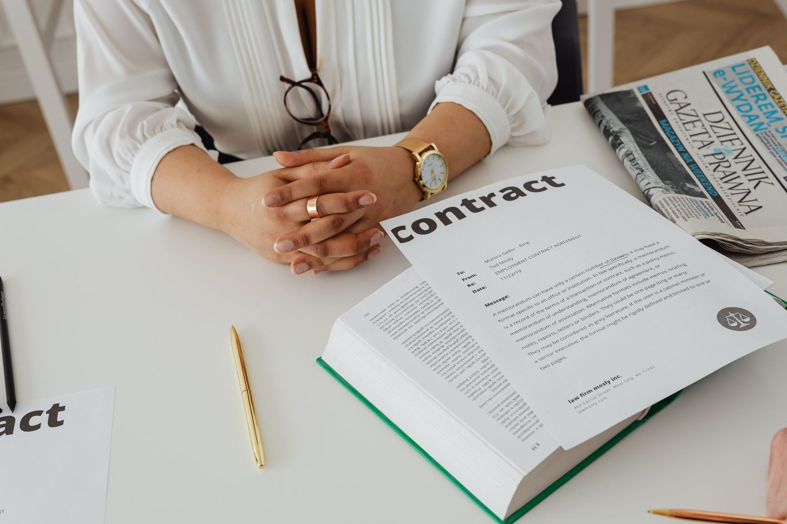 Mujer de negocios revisando un contrato en un escritorio junto a documentos legales y un periódico.