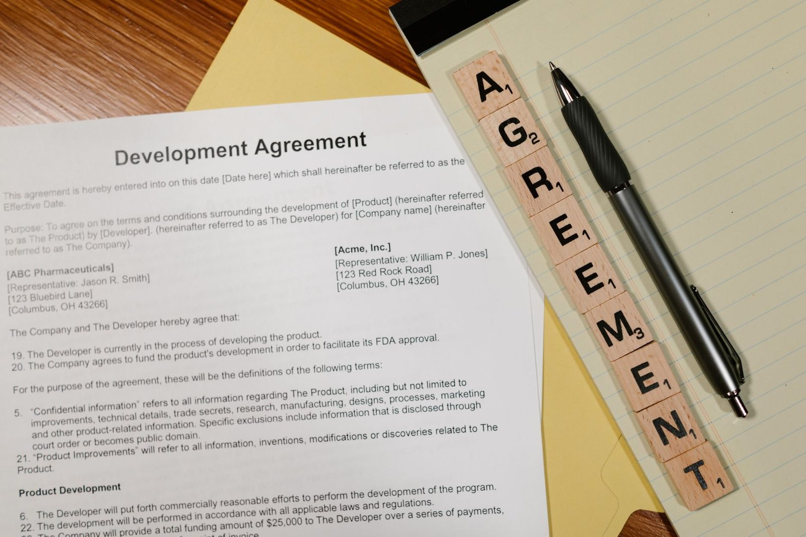 Close-up of a contract with a pen resting on it, and Scrabble tiles spelling "AGREEMENT" beside it.