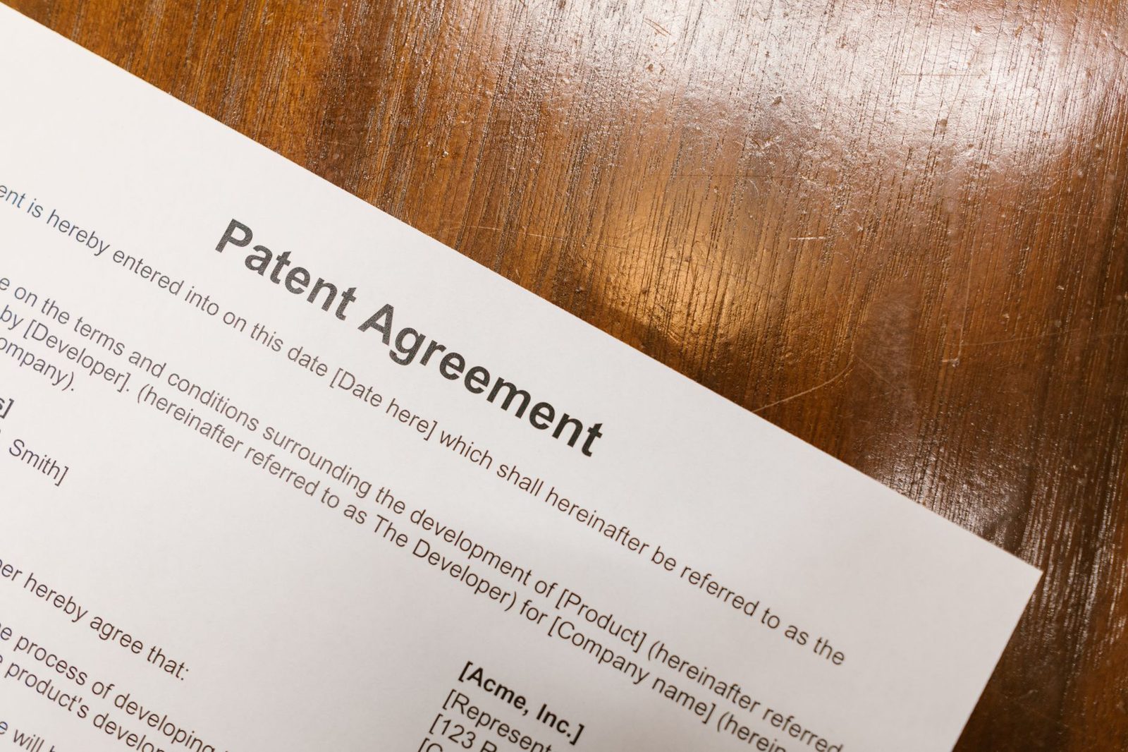 Close-up of a patent agreement document lying on a polished wooden table.