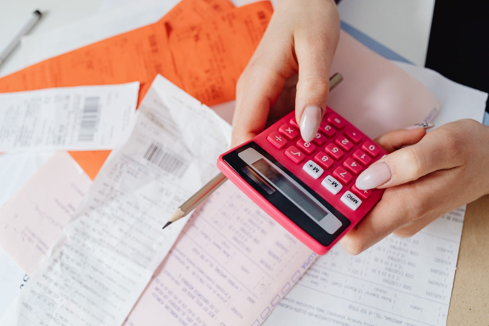 Hands using a pink calculator beside scattered receipts and financial documents.