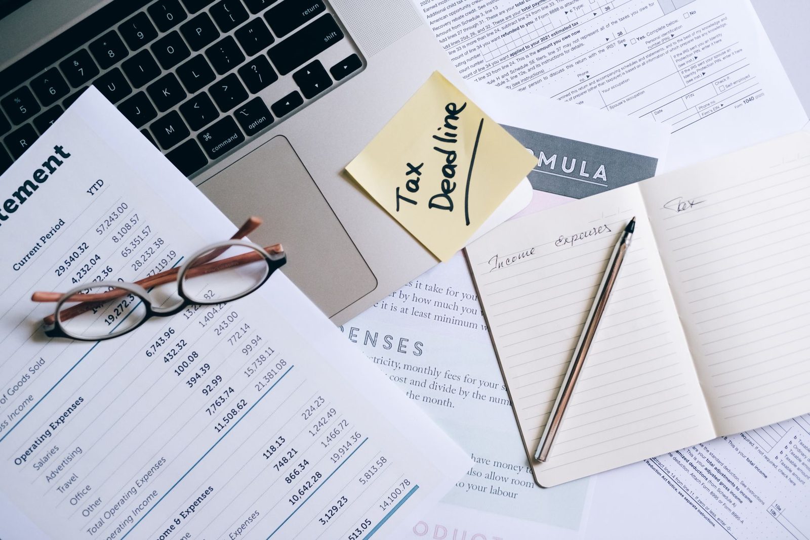 Laptop, documents, and a tax deadline note on a desk, representing financial management work.