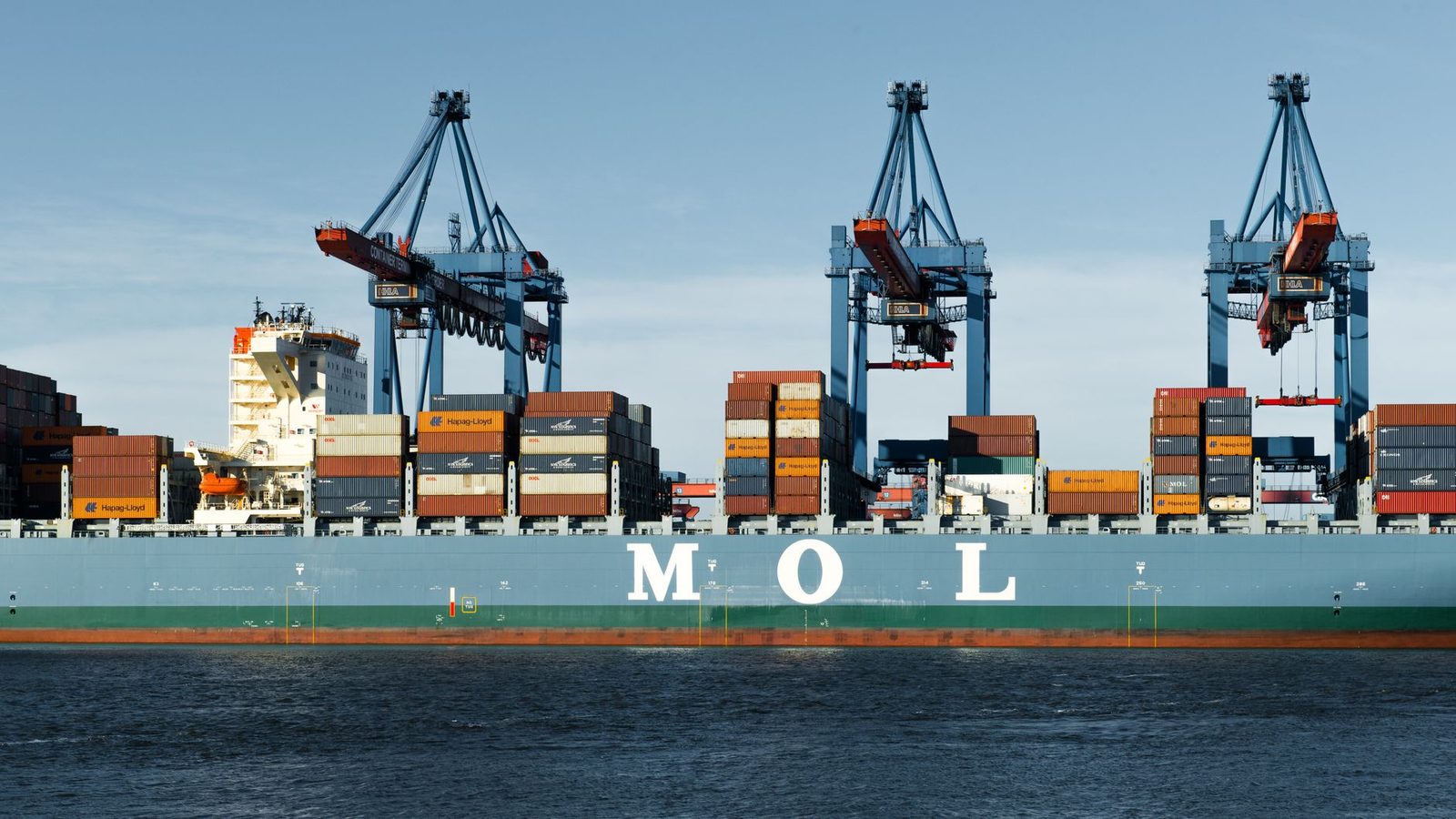 Large container ship moored at a Hamburg port terminal beside tall cranes.