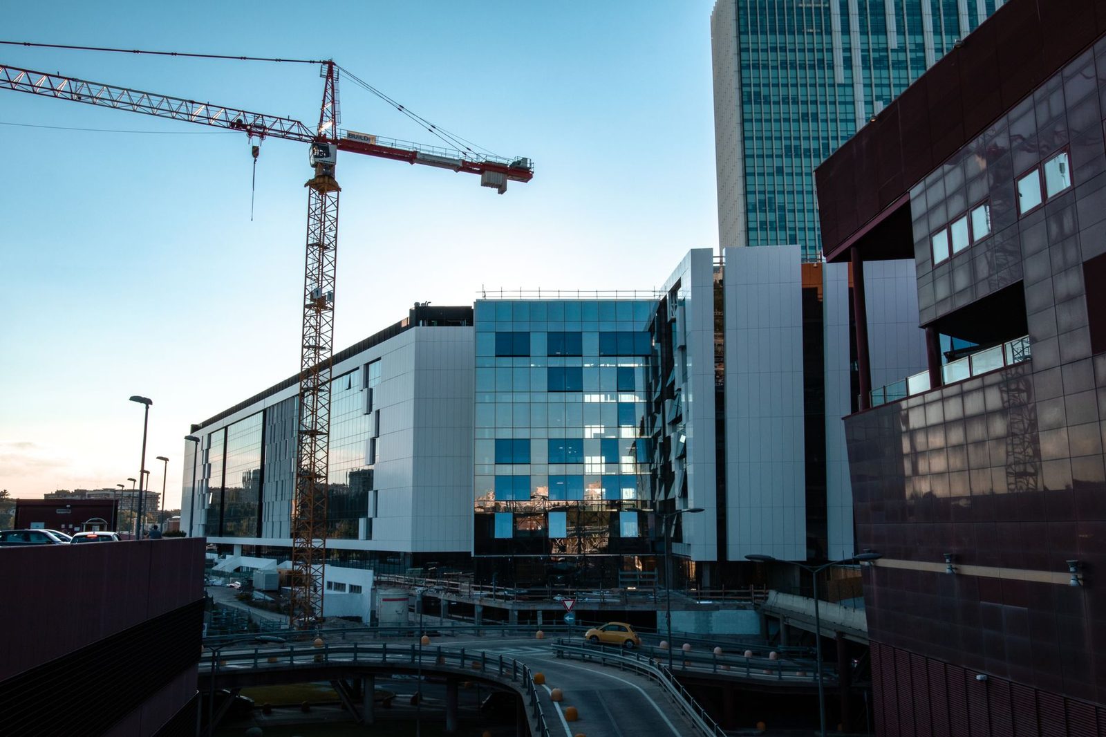 Modern high-rise under construction with cranes rising above a city skyline.