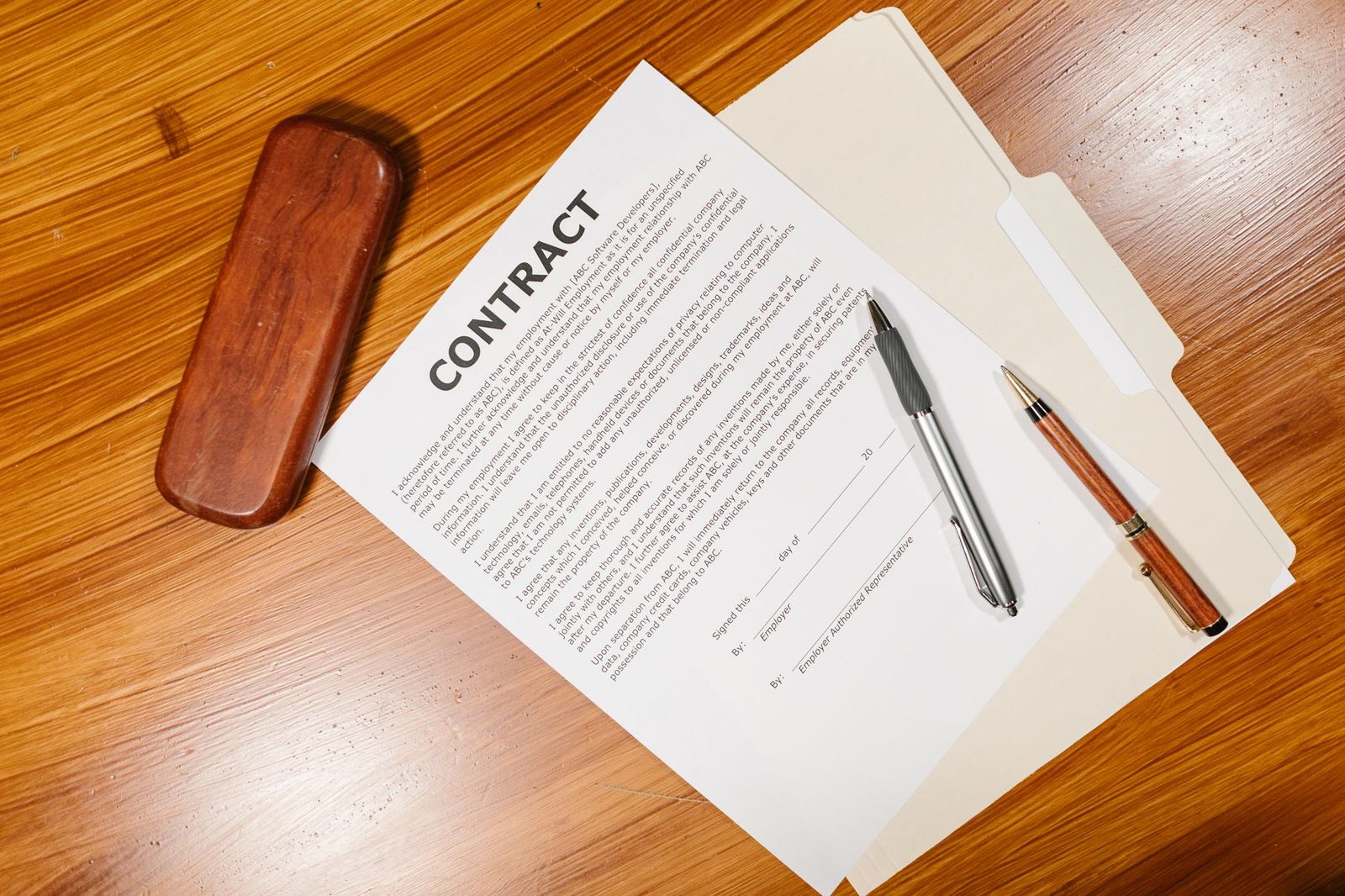 Overhead view of a signed contract, pens, and a briefcase on a wooden desk.