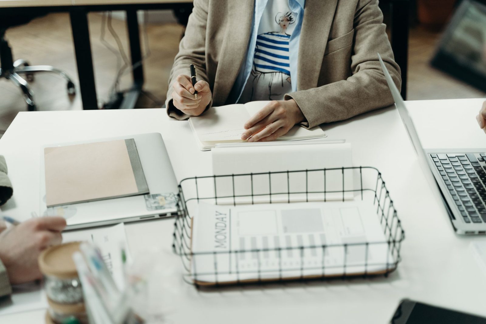 Person taking notes at a desk in a professional office, with papers and a laptop in view.