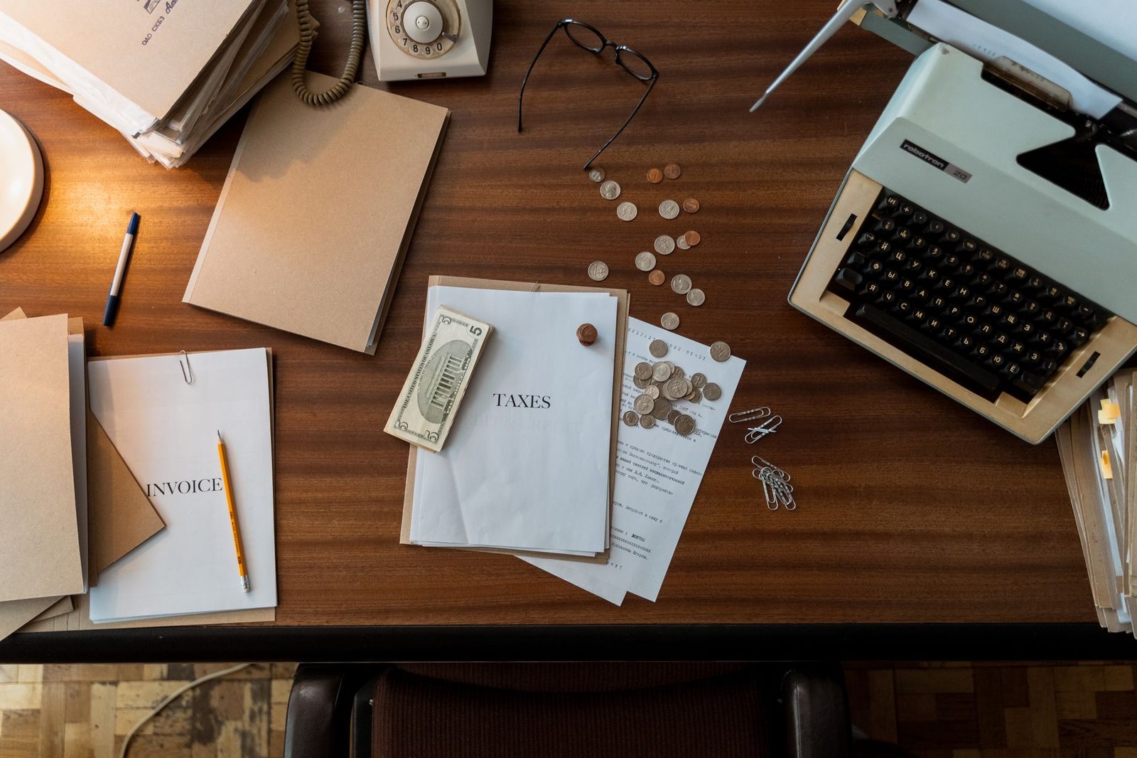 Escritorio de madera retro con una máquina de escribir, monedas sueltas y documentos legales dispersos.