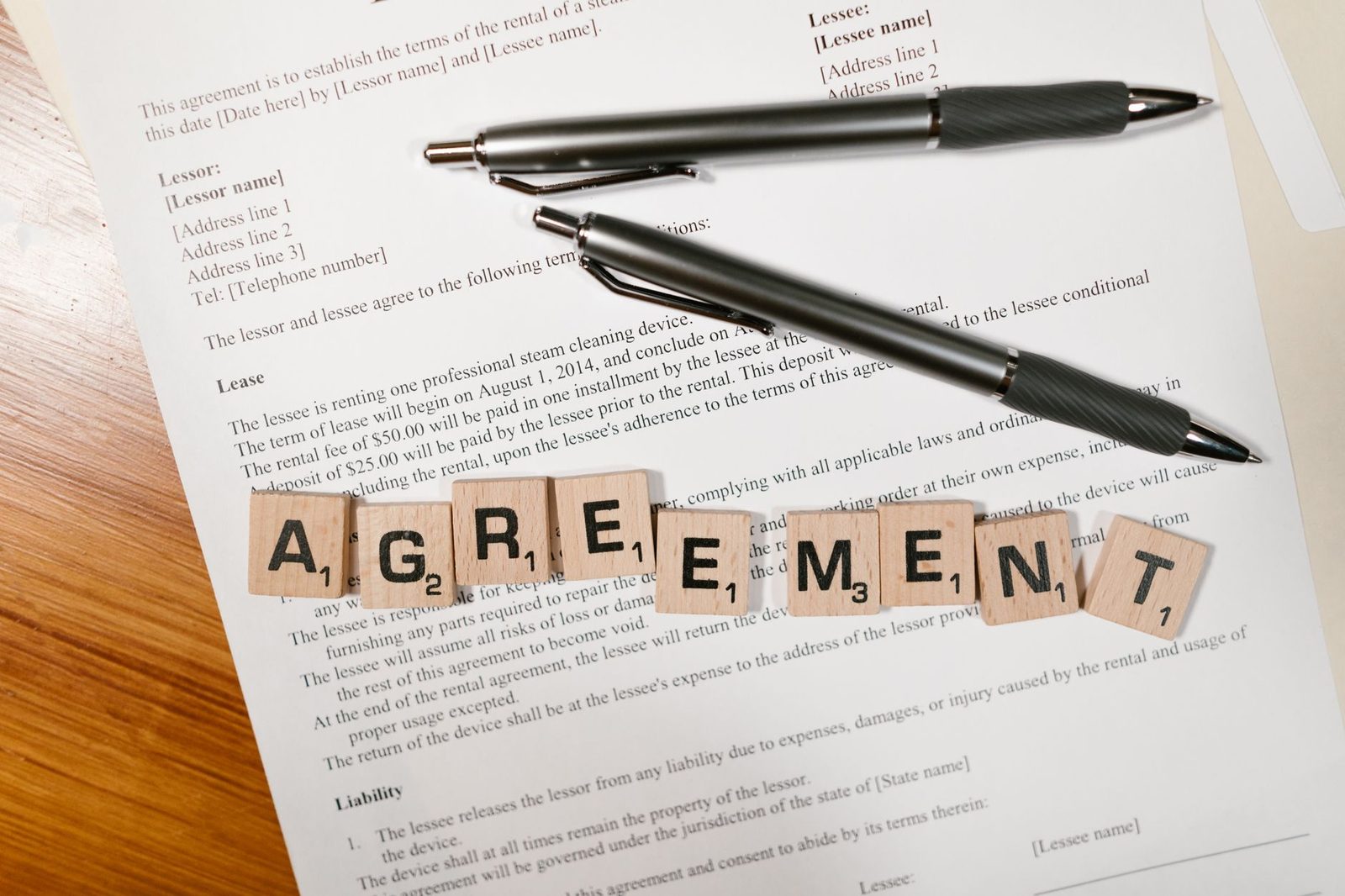 Scrabble tiles spelling "AGREEMENT" beside two pens on a document, symbolizing contract signing