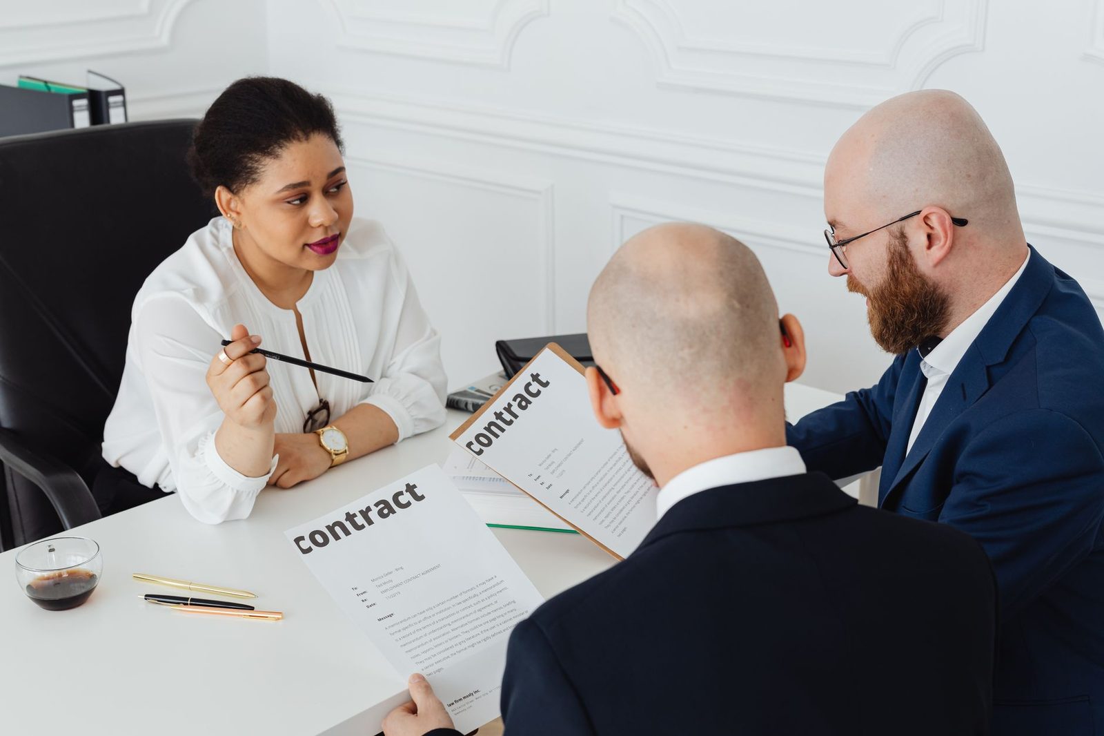 Three business professionals discuss a contract across a desk in a modern office.