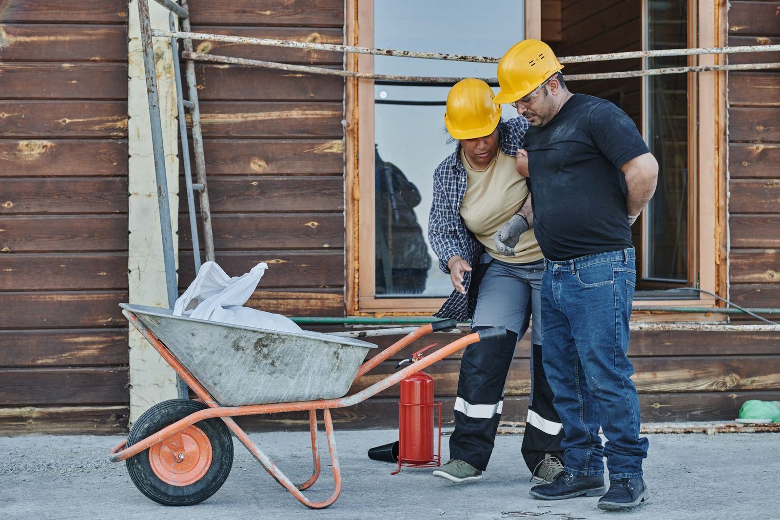 Two construction workers in hard hats help an injured colleague at a job site, illustrating workplace safety.