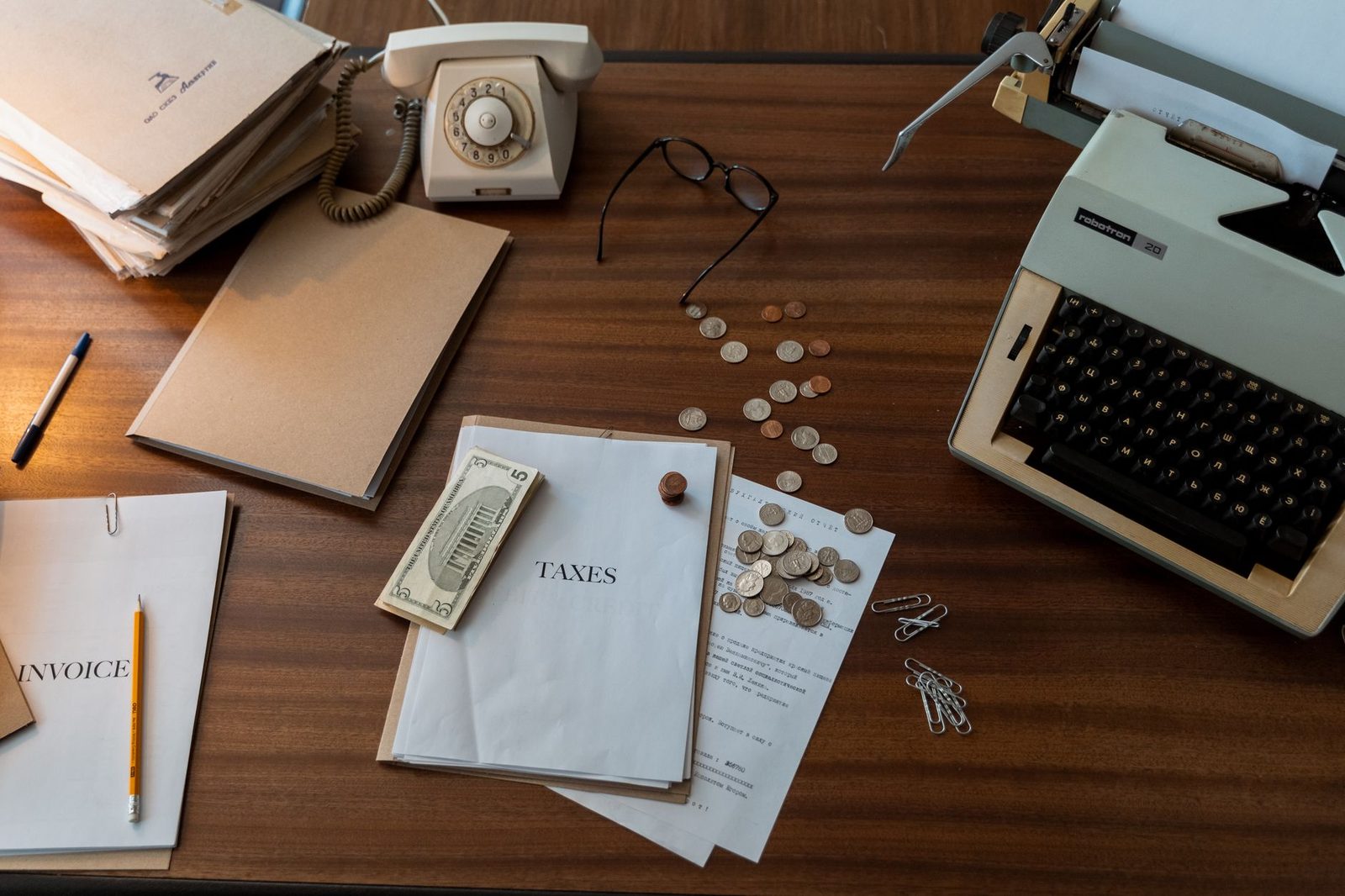 Escritorio de madera antiguo con una máquina de escribir, documentos apilados y un teléfono clásico.