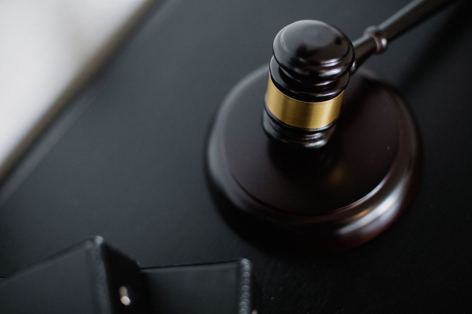 Wooden gavel resting on a round surface beside case folders on a table in a courtroom, viewed from above.