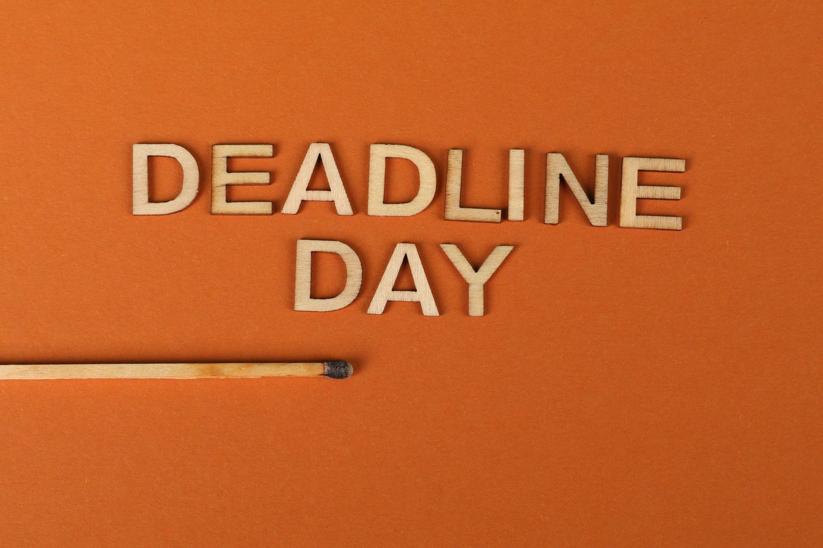 Wooden letters spelling a deadline word beside a burnt matchstick against an orange background.